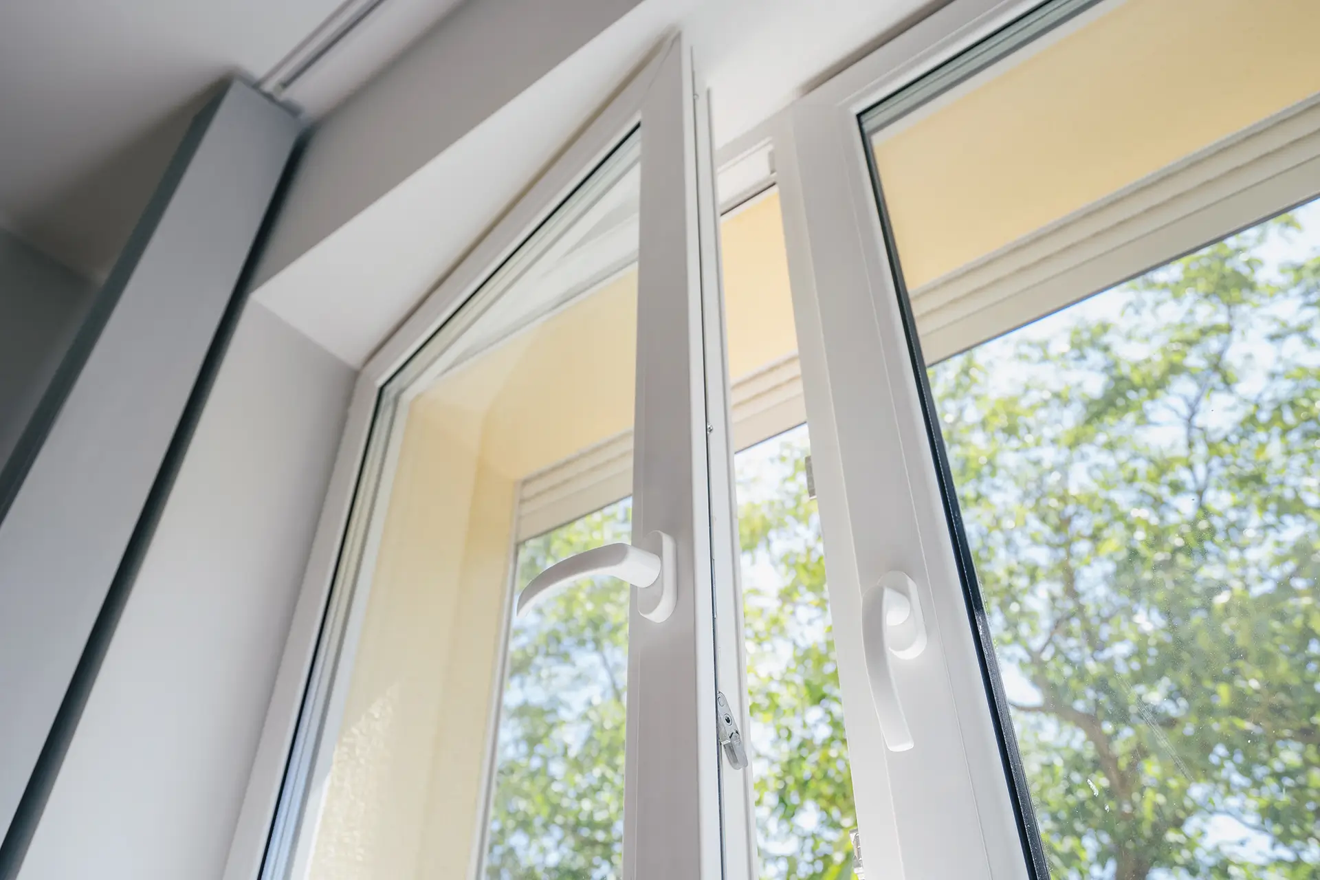 Fenster auf Kipp mit einem blühenden, grünen Baum dahinter